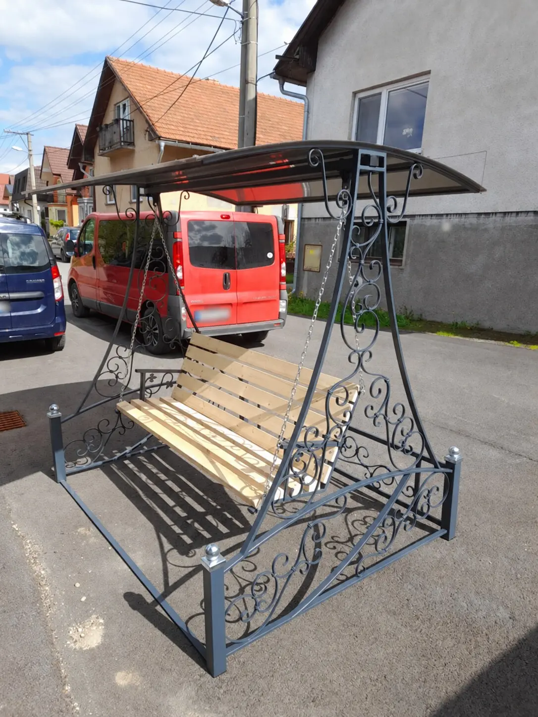 Kovaná hojdačka s drevenou lavicou zachytená z bočného uhla